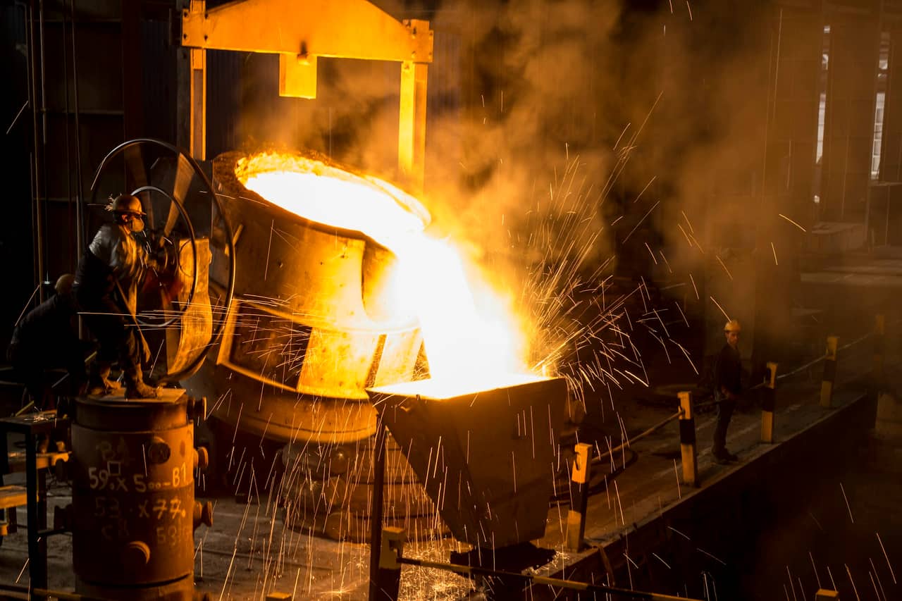 Molten metal being poured at a steelworks, glowing orange against dark machinery.